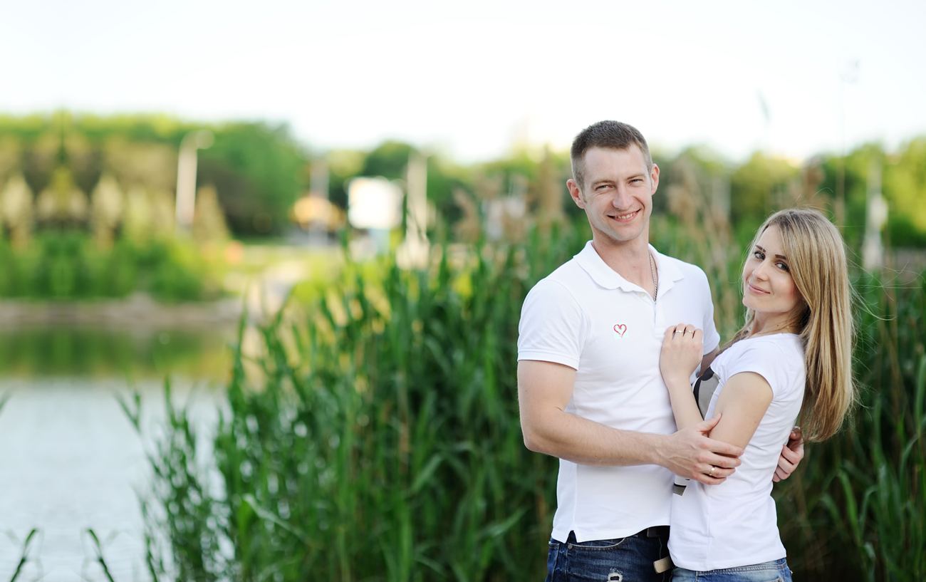 A smiling couple standing together outdoors by a lake